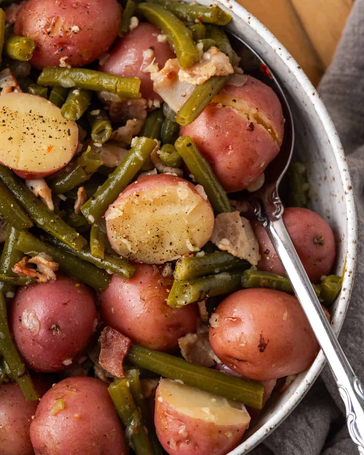 A serving bowl of small red potatoes and green beans topped with pieces of bacon. 