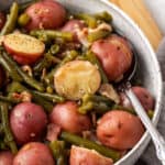 A serving dish of green beans and potatoes with bacon.