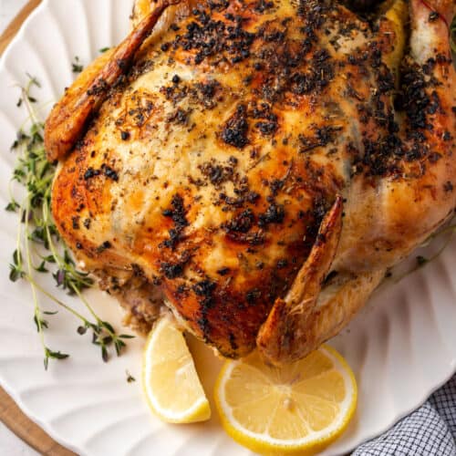 An herb roasted chicken on a white serving platter.
