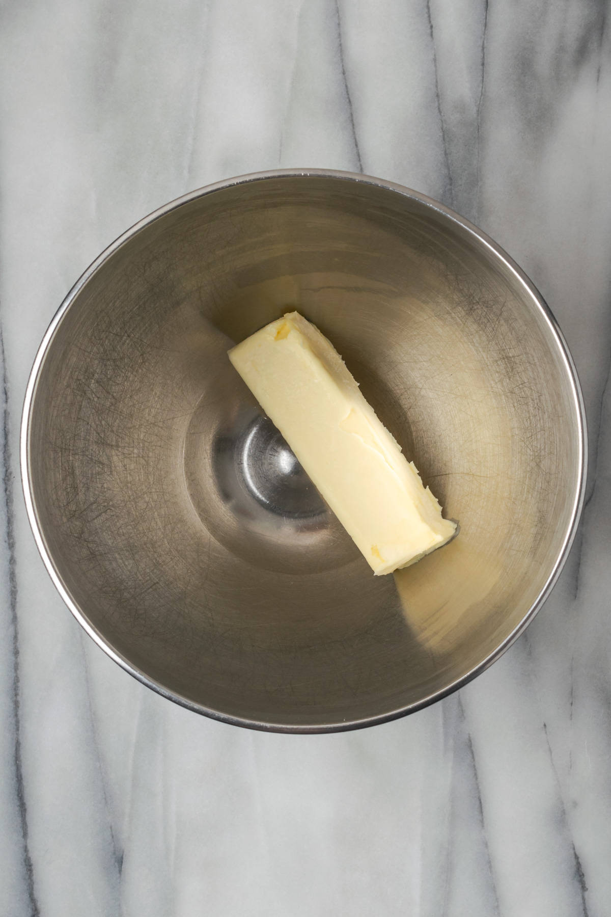 A stick of butter in the bowl of a stand mixer.