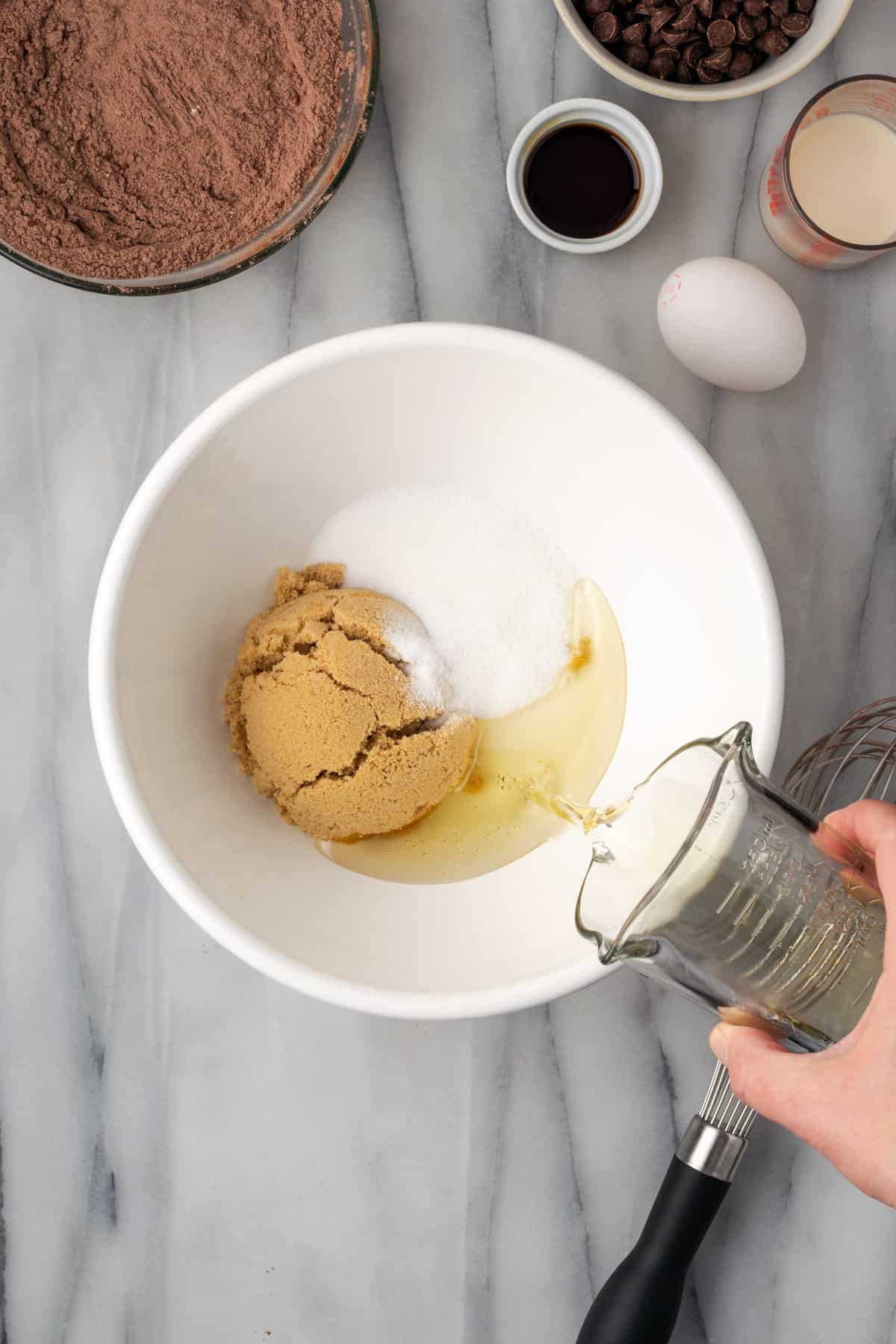 White sugar, brown sugar and oil  combined in a large white mixing bowl.