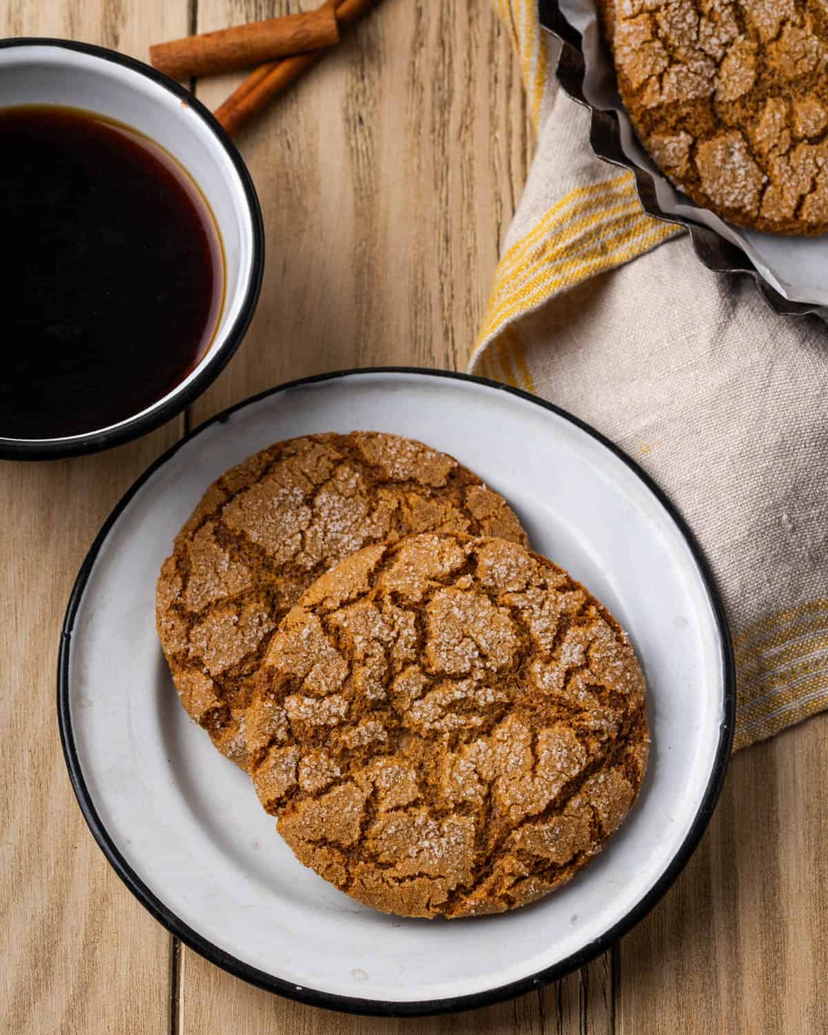 Two gluten free molasses cookies served on a small white plate with a cup of coffee.