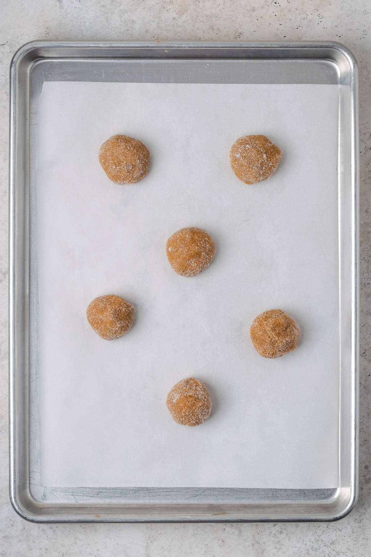 Six balls of molasses cookie dough sitting on a baking tray.