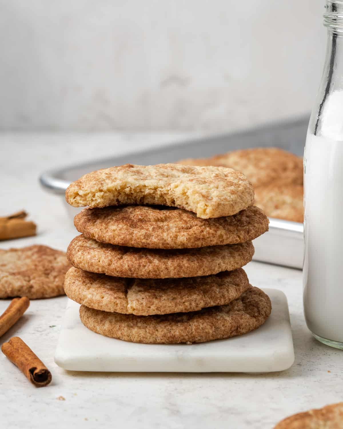 A stack of snickerdoodle cookies sitting next to a jar of milk on a white table.