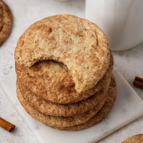 A stack of gluten free snickerdoodles with one cookie missing a bite.