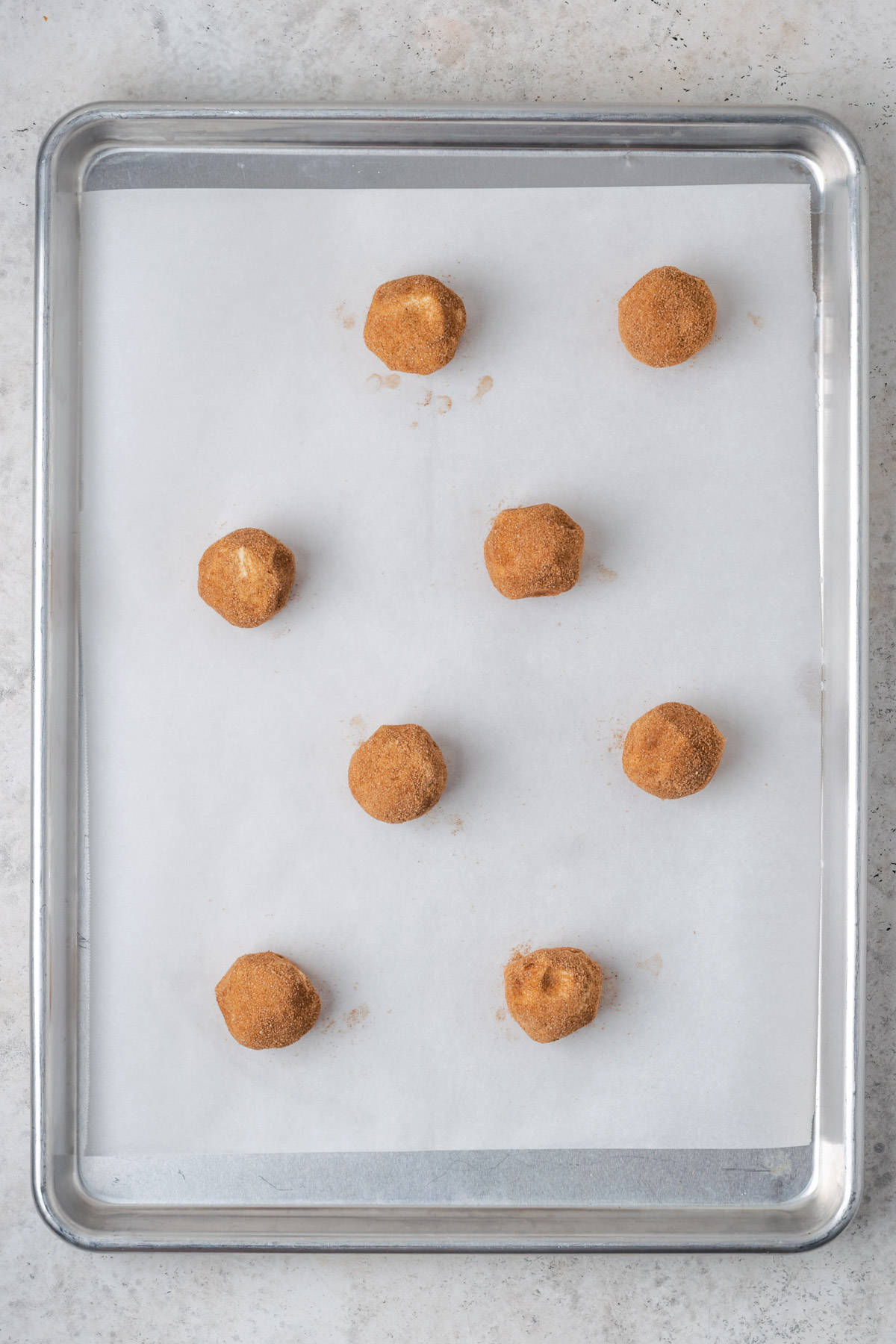 Eight unbaked snickerdoodle cookie dough balls on a baking sheet. 