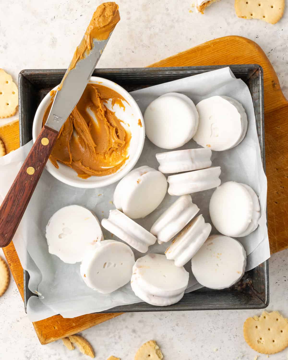 White chocolate covered Ritz cracker cookies sitting in a baking dish next to a bowl of peanut butter.