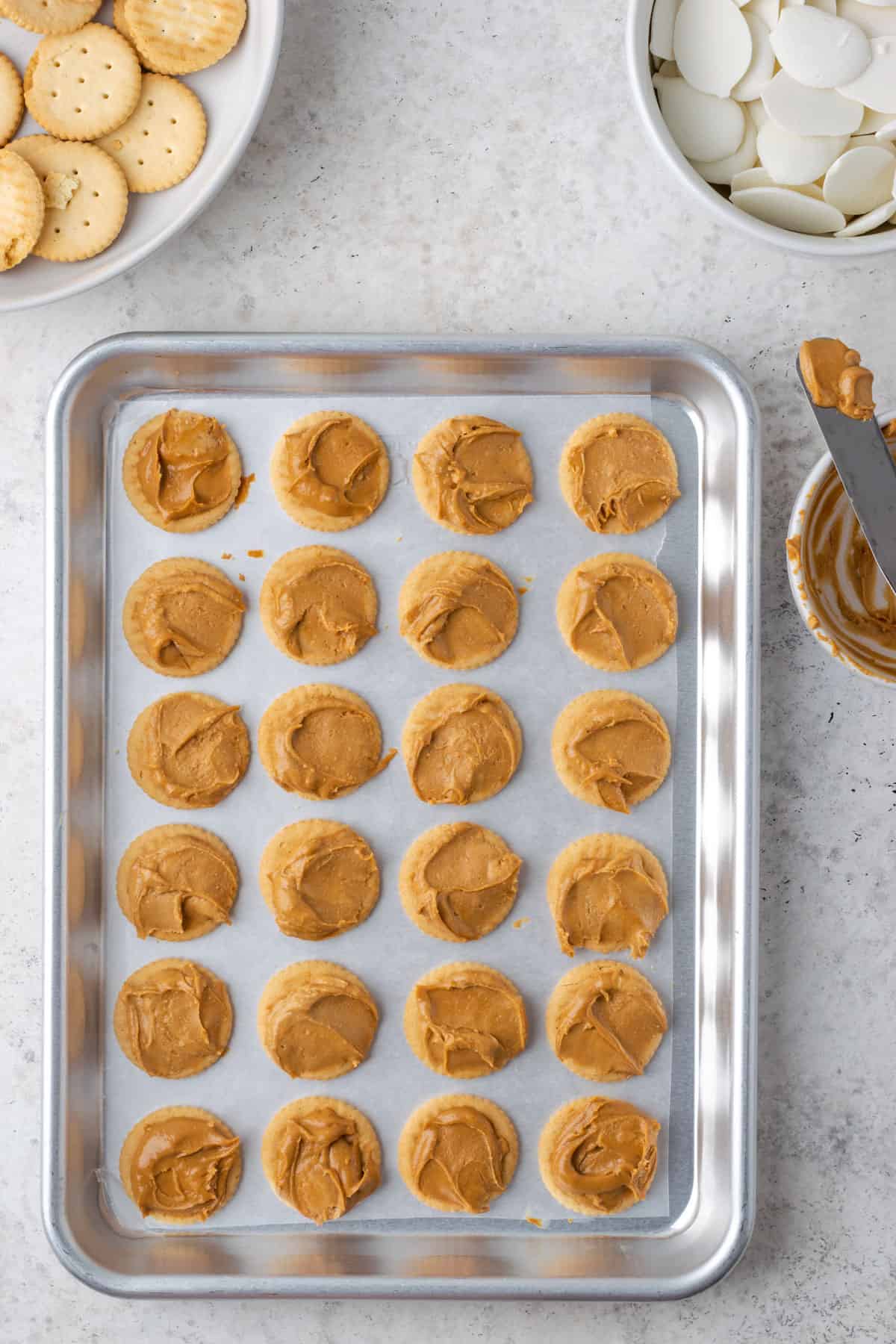24 Ritz crackers with peanut butter spread on top laying on a baking tray.
