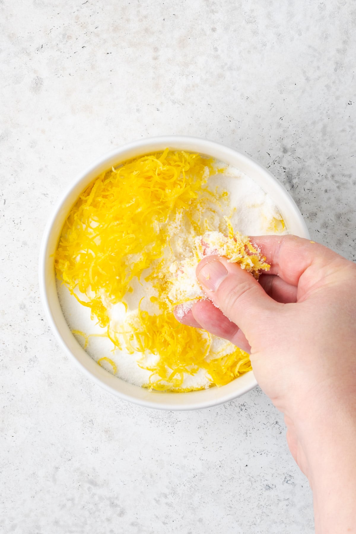 Lemon zest being rubbed into sugar in a small white bowl. 