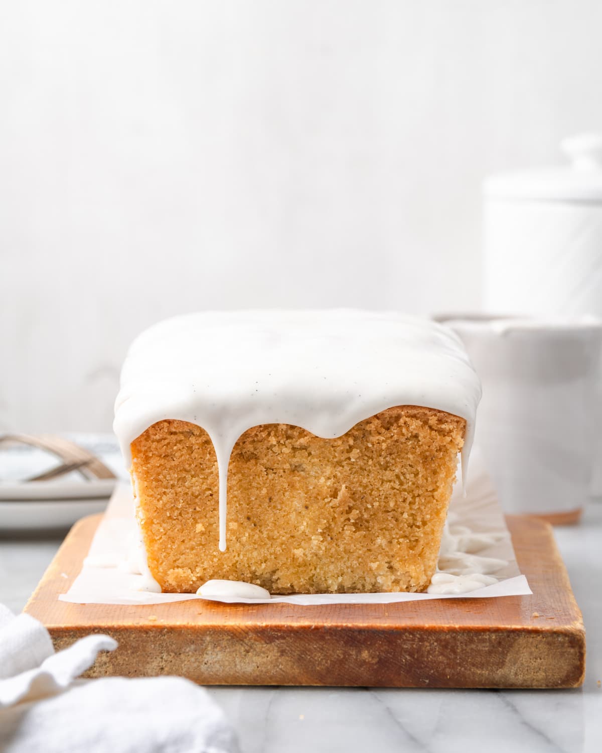 A gluten free pound cake topped with vanilla icing sitting on a cutting board.