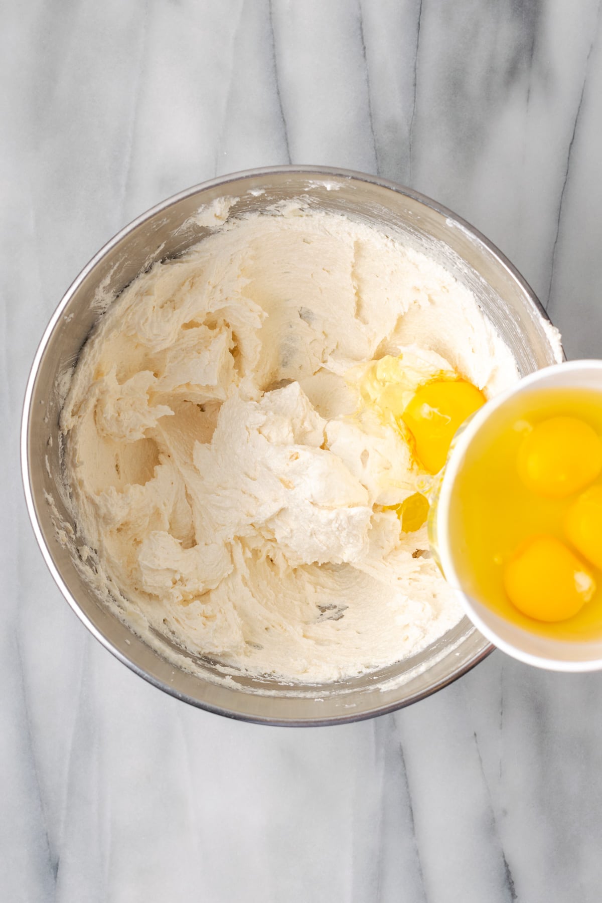 Eggs being added one at a time to the mixing bowl. 