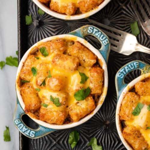 Small crocks filled with Mexican tater tot casserole topped with melted cheese.