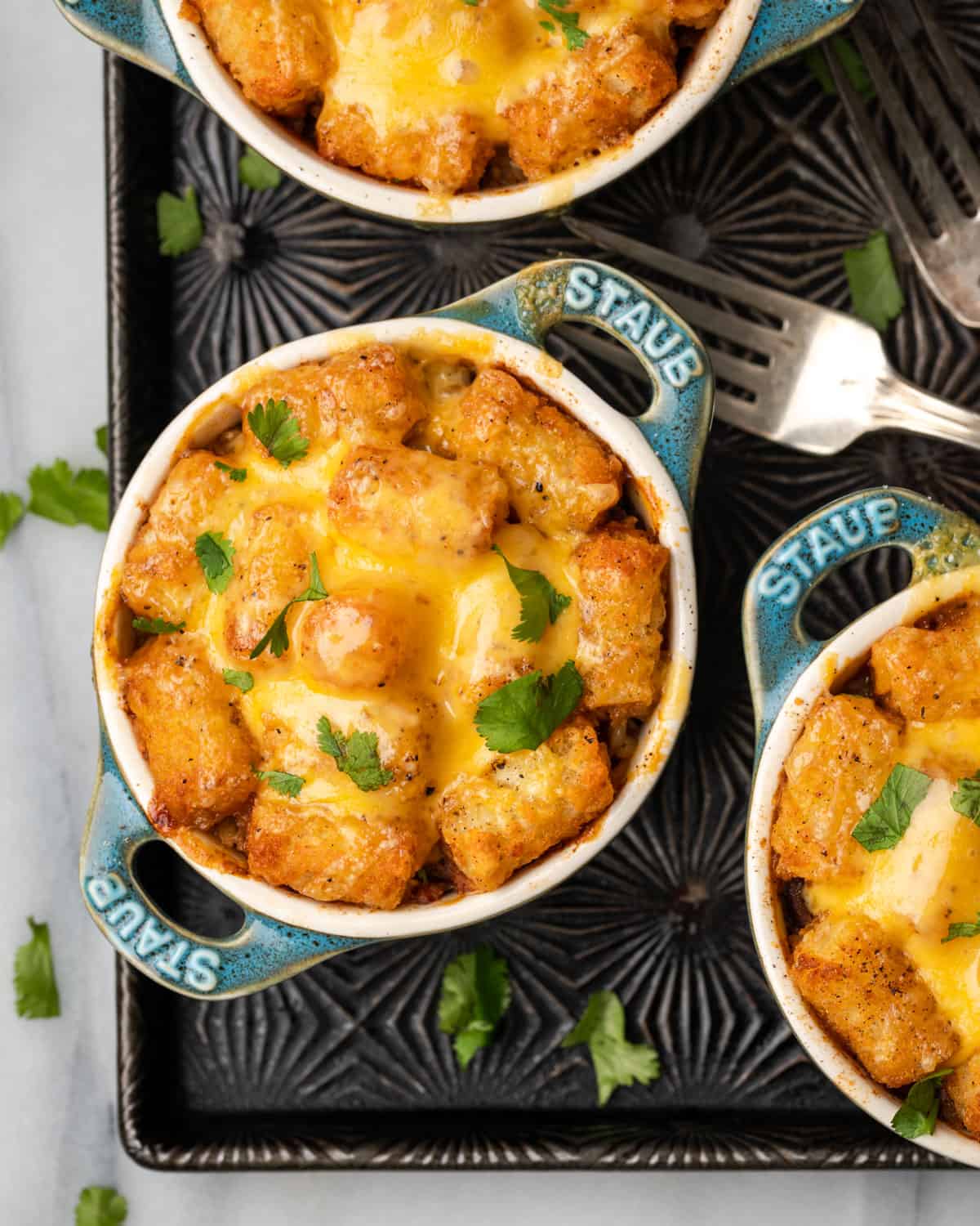 Three small dishes of tater tot casserole sitting on a baking tray.