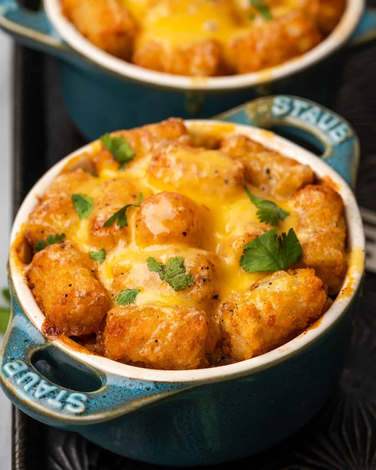 Mexican tater tot casserole topped with melted cheese and served in an individual ceramic crock.