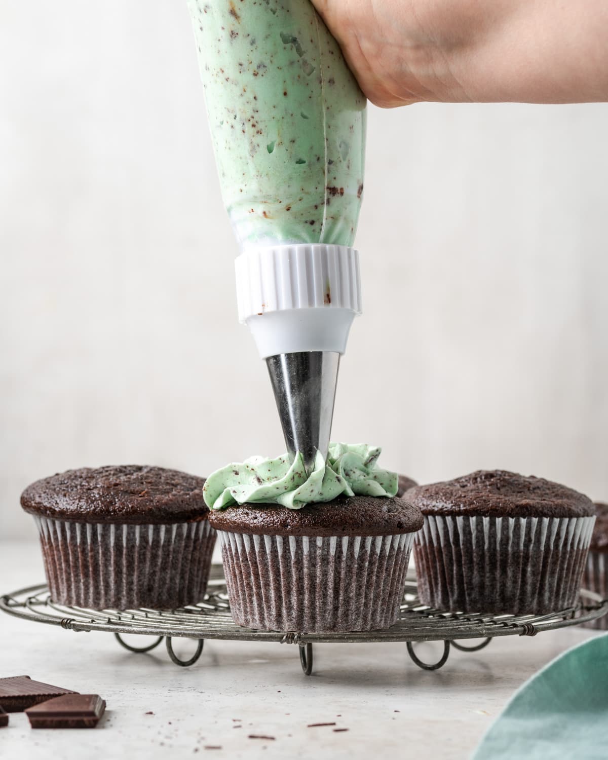 A chocolate cupcake being topped with mint chocolate chip frosting.