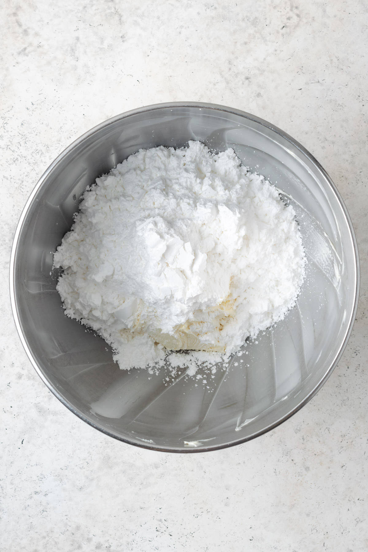 Powdered sugar being added to the mixing bowl with the creamed butter.