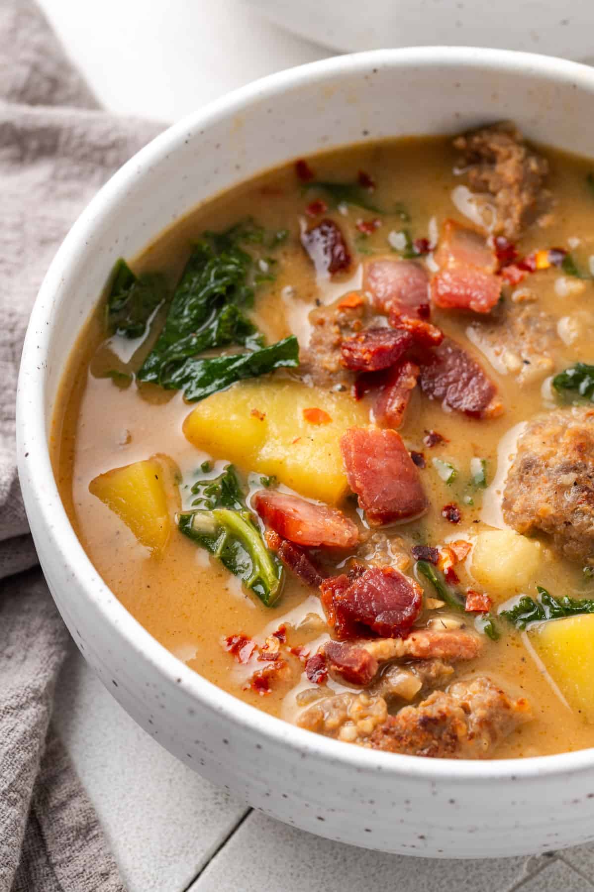 A bowl of zuppa toscana soup topped with bacon pieces.