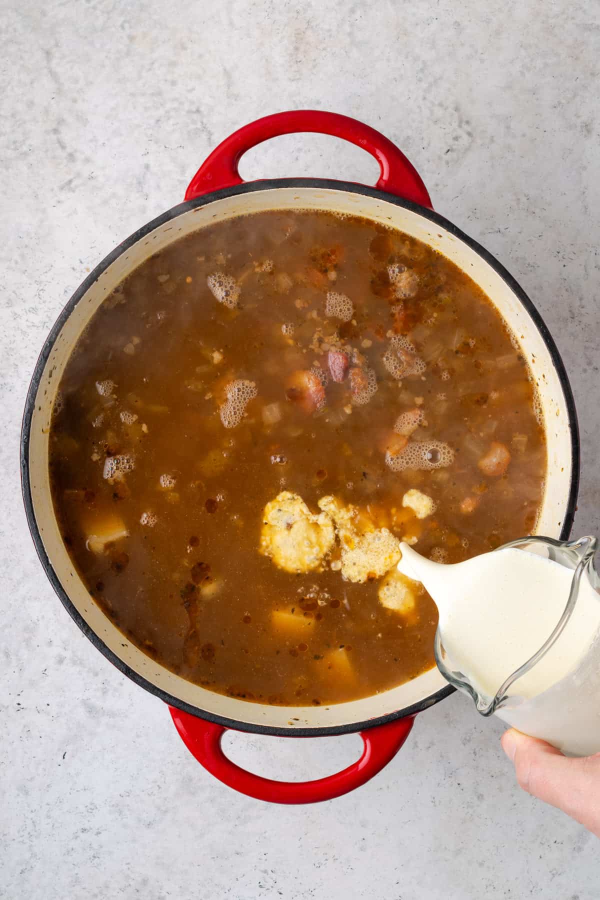 Sausage, bacon and cream being added to the partially cooked soup.