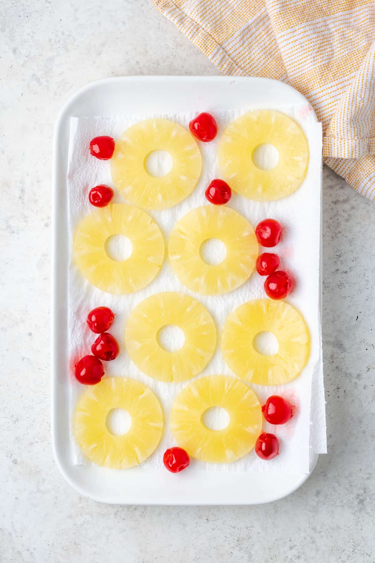 Pineapple slices and cherries spread on a platter lined with paper towels.