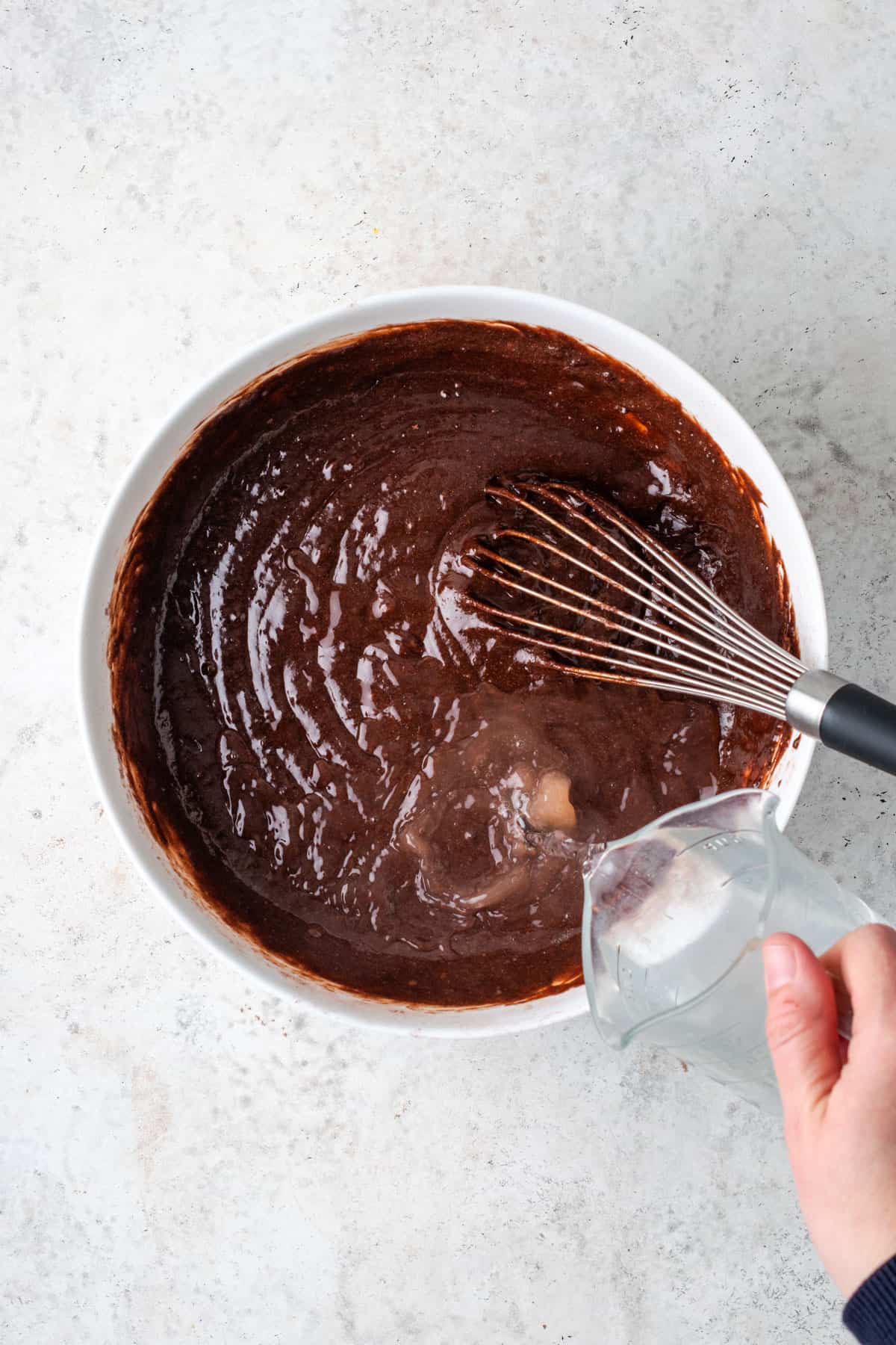 Hot water being poured into the mixed chocolate cake batter.