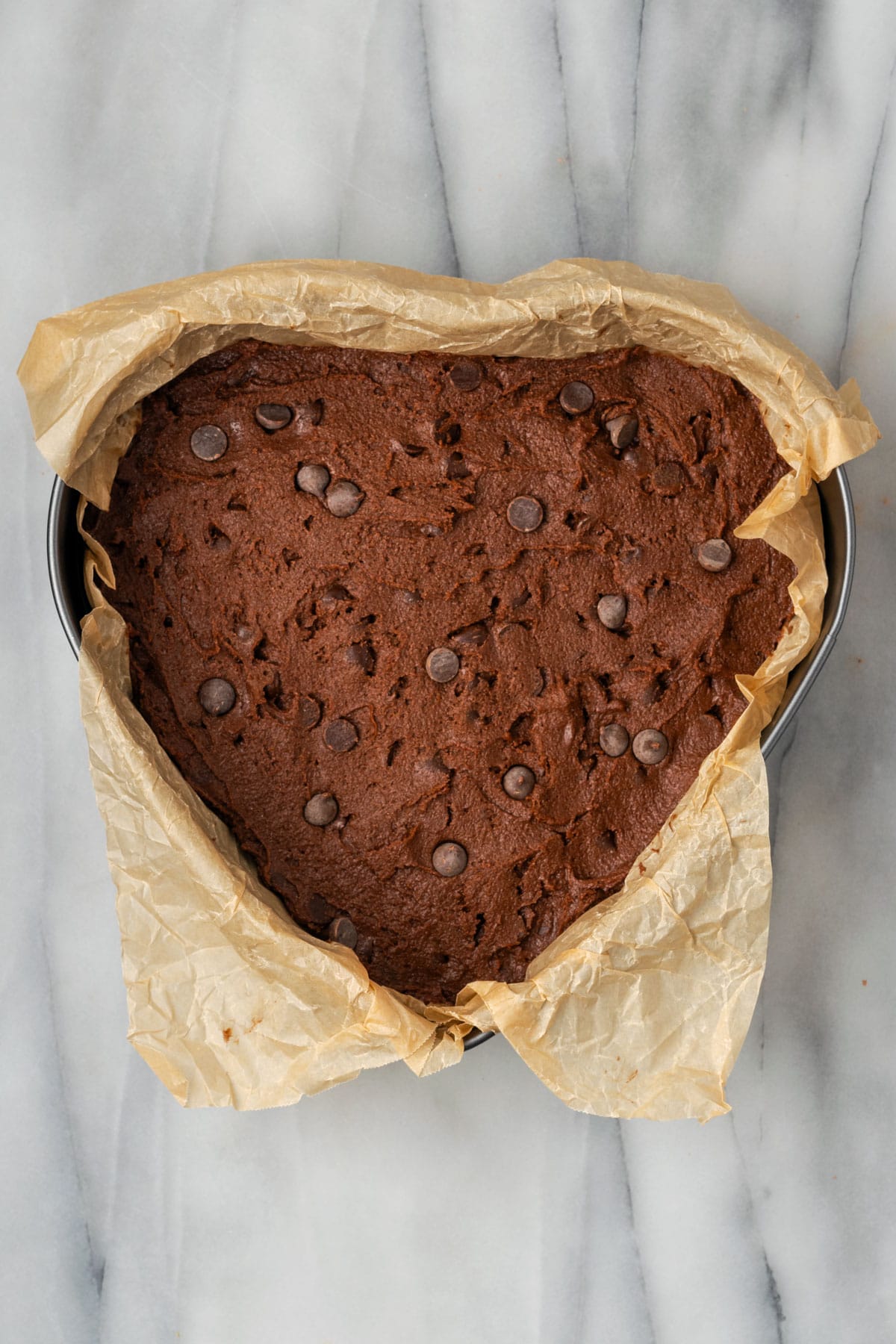 A heart shaped baking pan filled with unbaked chocolate chip cookie dough.