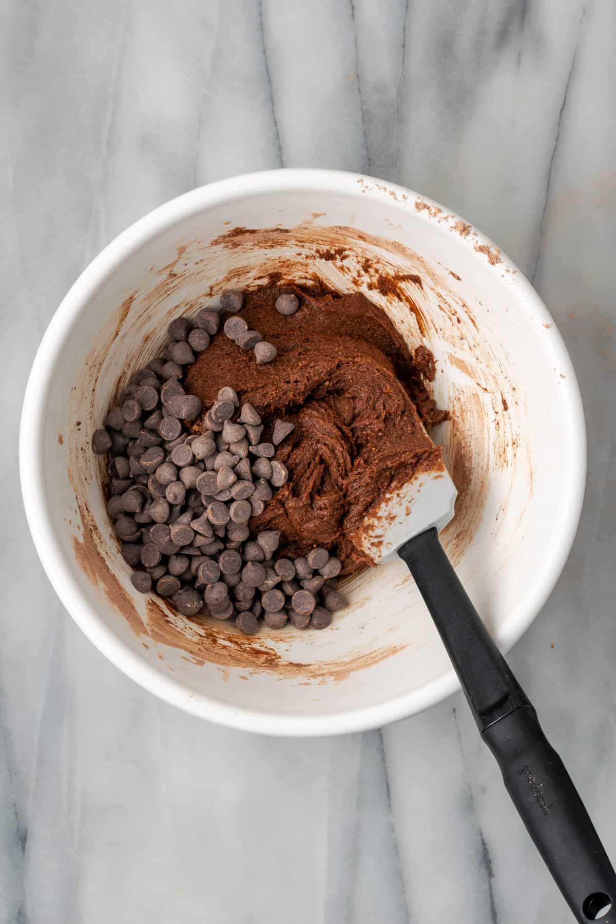 Chocolate chips being folded into the chocolate cookie dough with a spatula.