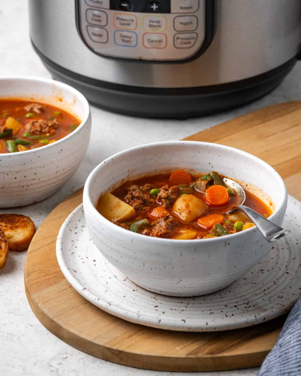 Two bowl of hamburger soup sitting on a white table next to an instant pot.