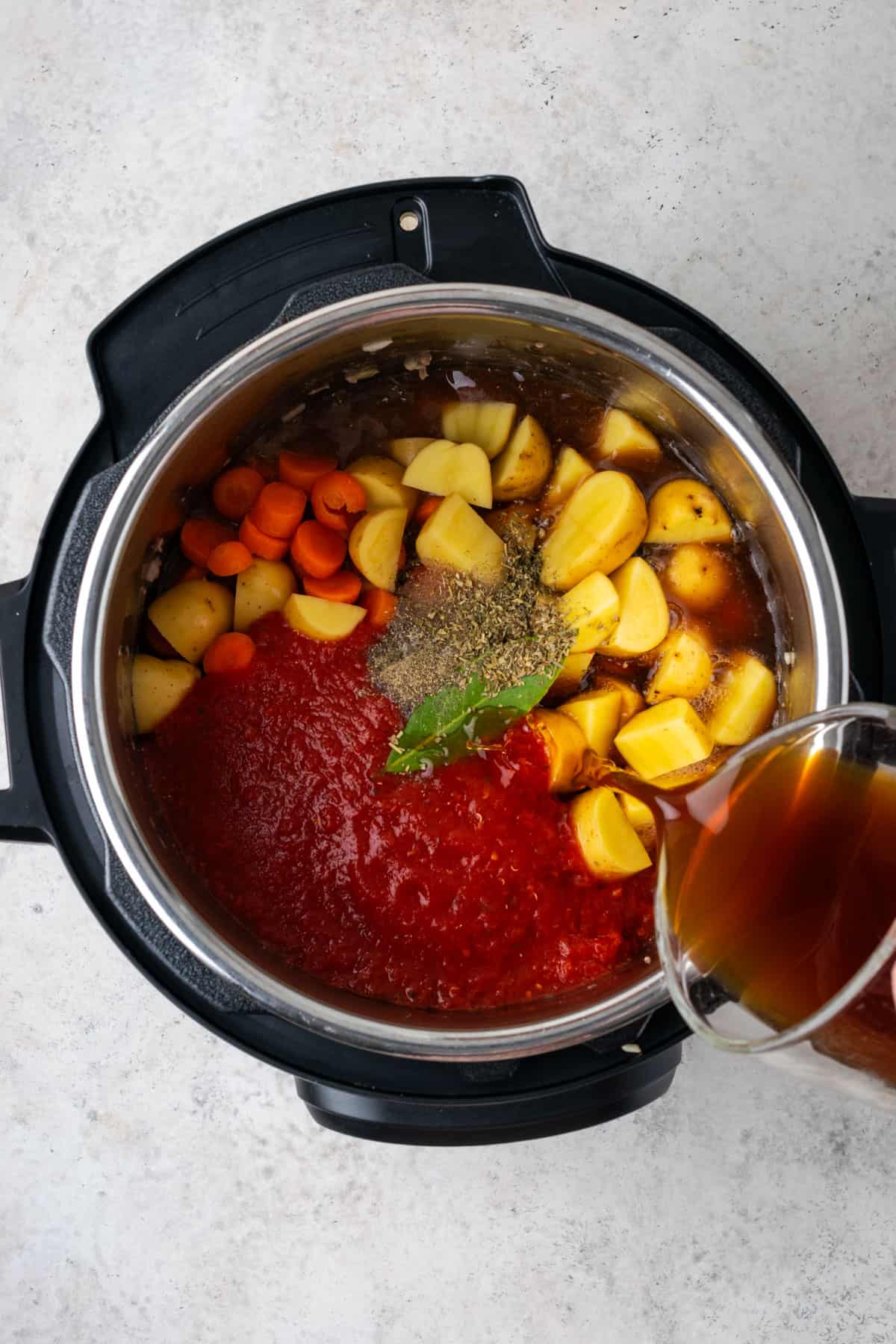 Fresh vegetables, tomatoes, beef broth and herbs being added to the instant pot.