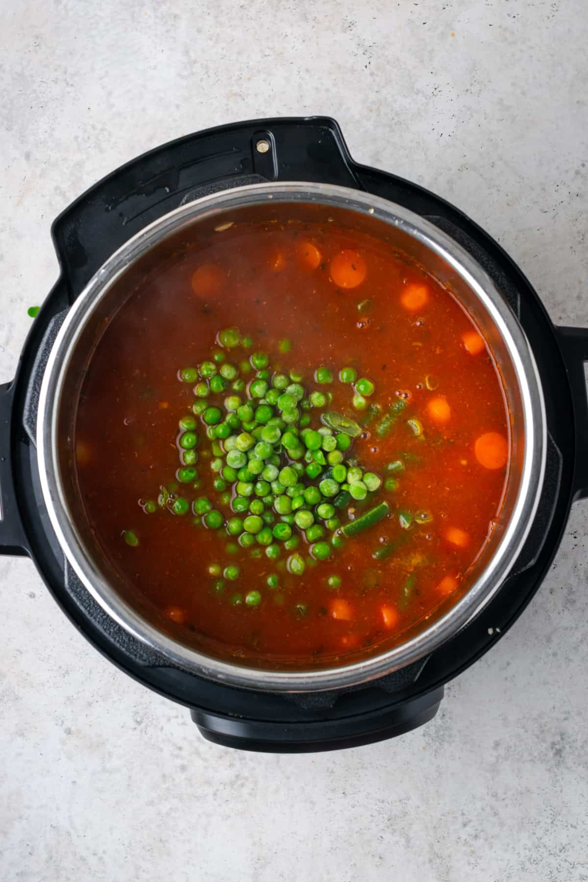 Frozen vegetables being added to the cooked hamburger soup inside the instant pot.