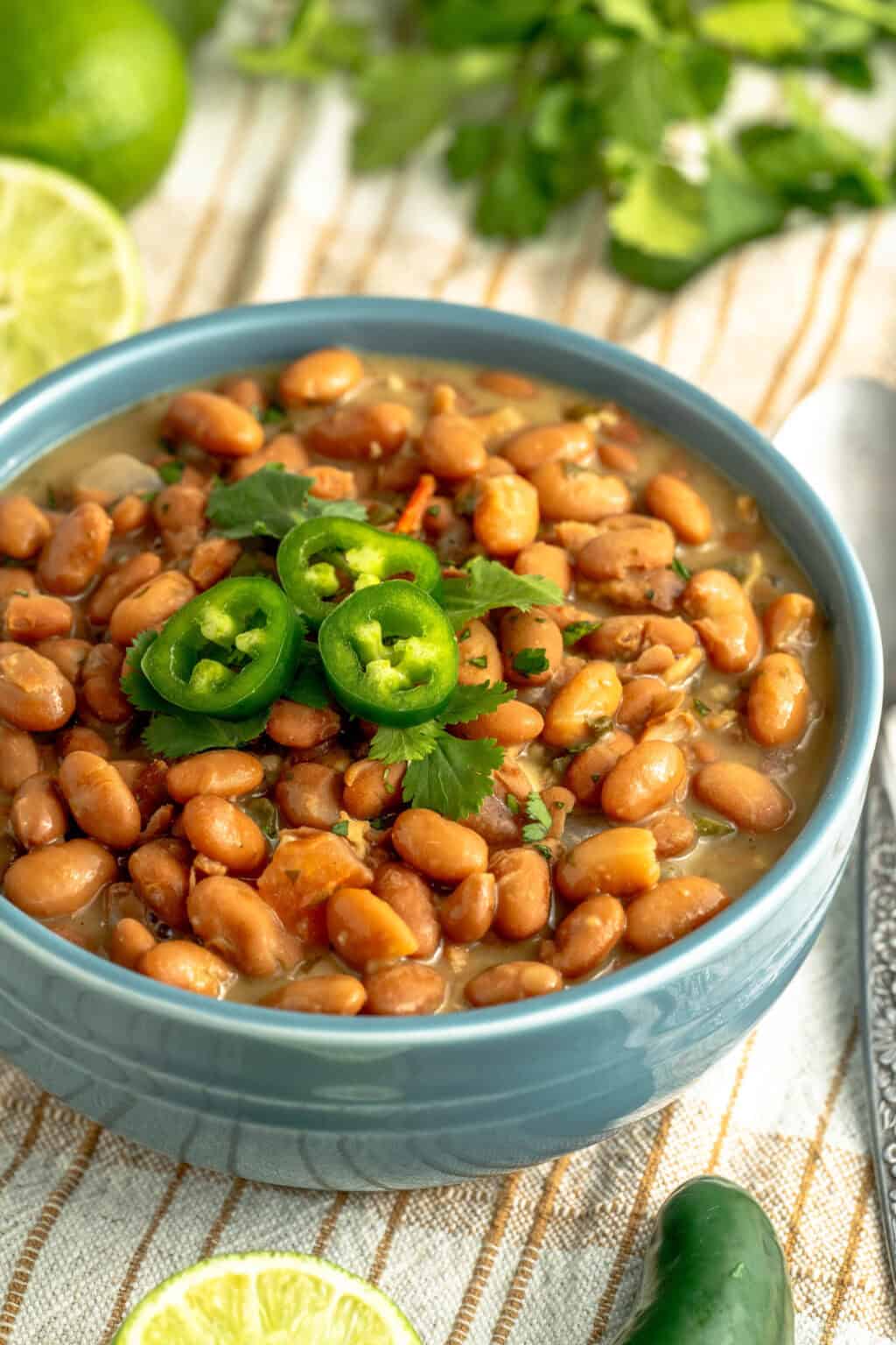 A bowl of charro beans topped with slices of fresh jalapenos.