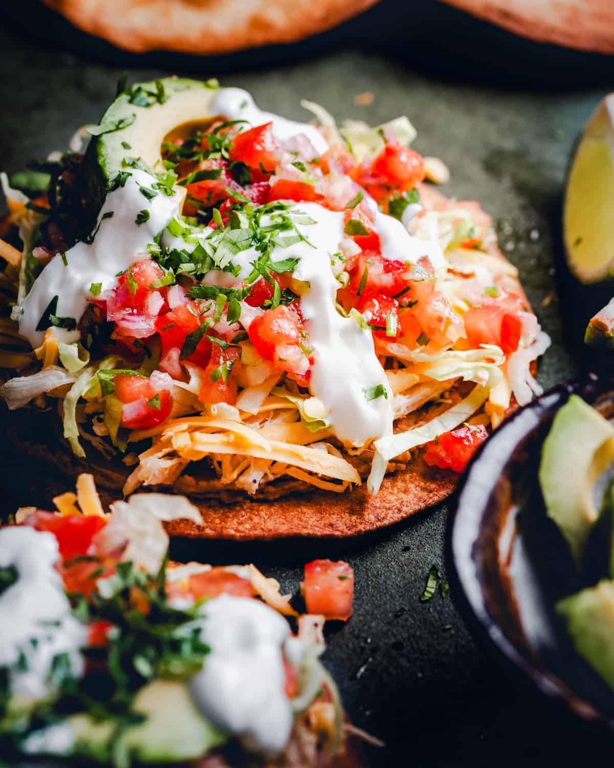A chicken tostada topped with cheese, sour cream and fresh tomatoes.