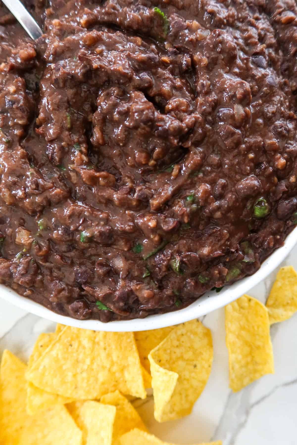 A bowl of refried black beans served with corn chips.