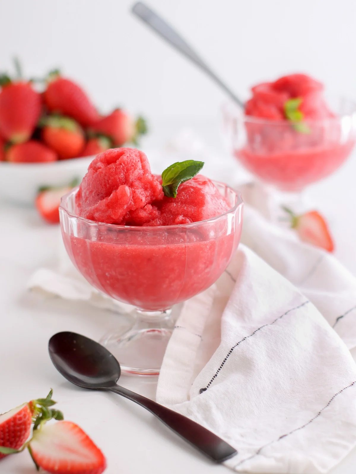 Two glass dishes of strawberry sorbet sitting next to a bowl of fresh berries.