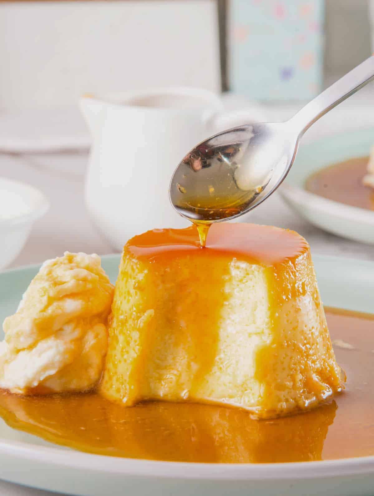 Caramel being poured over a serving of flan on a small plate.