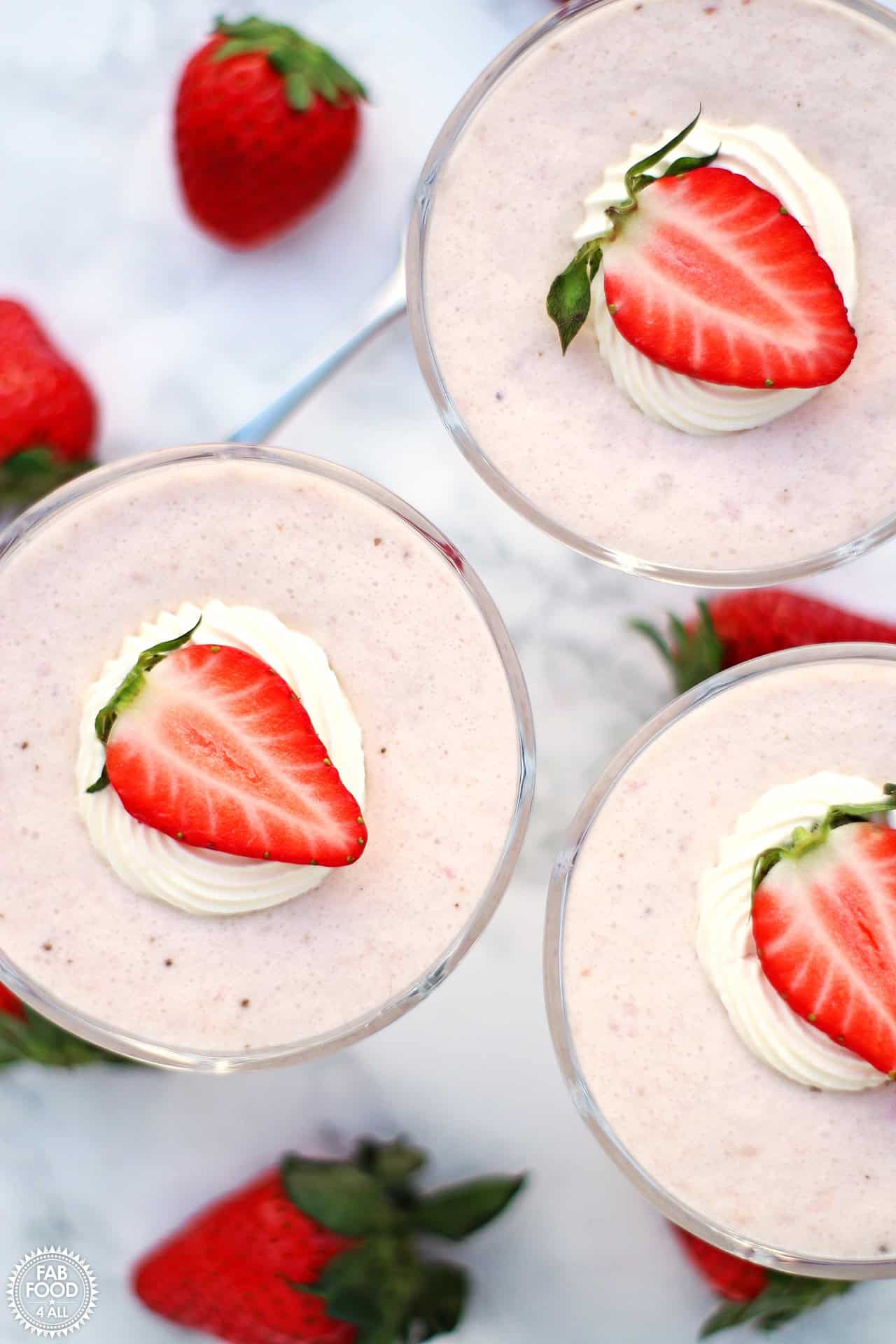 Three dishes of strawberry mousse topped with whipped cream and fresh berry slices.