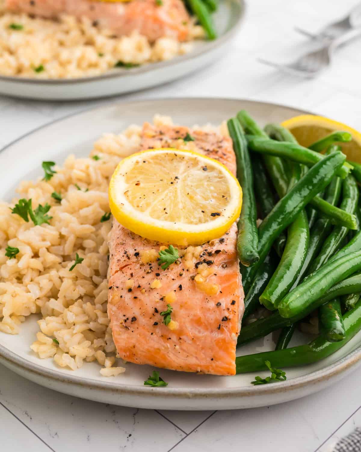 A lemon pepper salmon filet served with brown rice and green beans on a white plate.