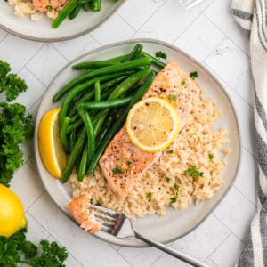 Lemon pepper salmon served on a white plate with brown rice and green beans.