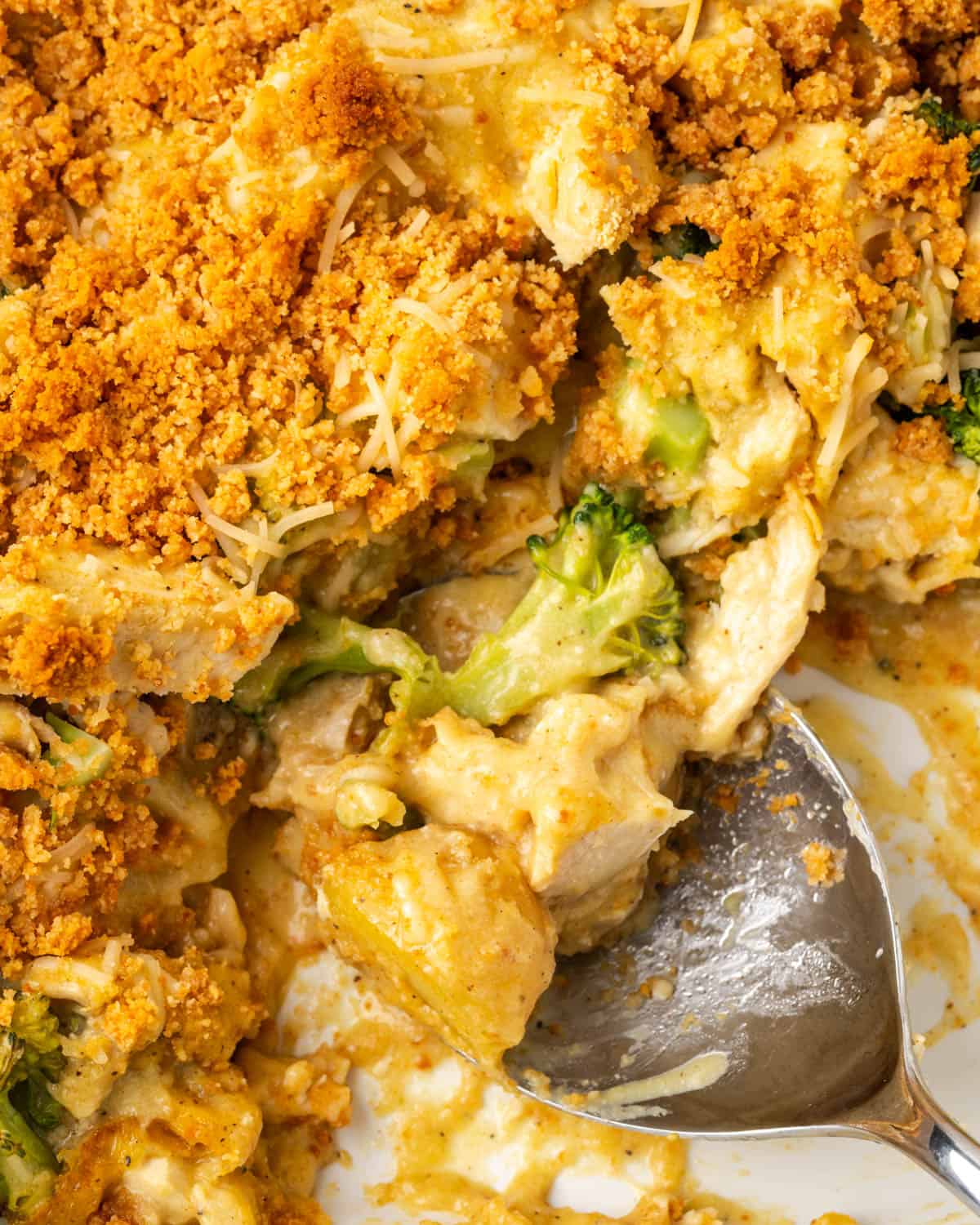 A serving spoon scooping out a serving of chicken broccoli potato casserole.