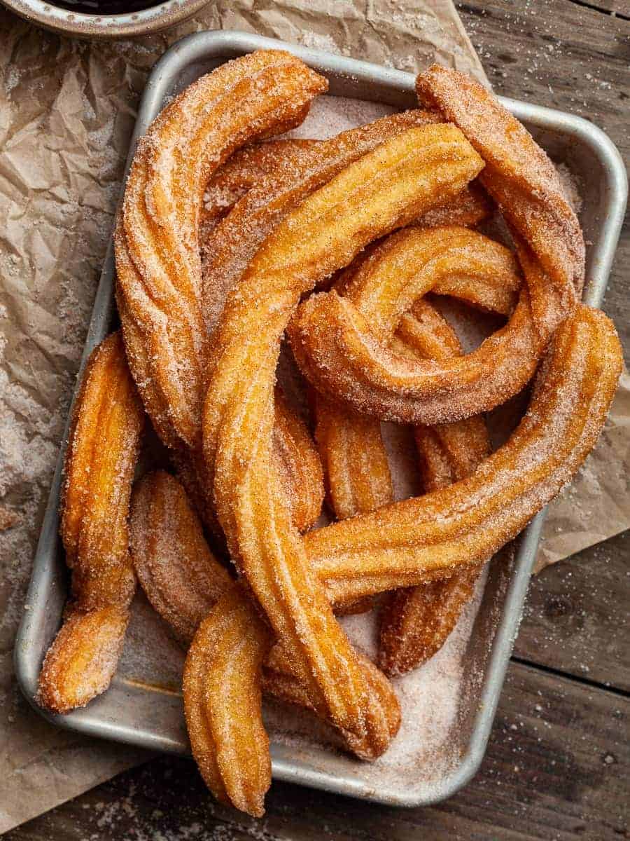 A pile of gluten free churros sitting on a metal baking tray.