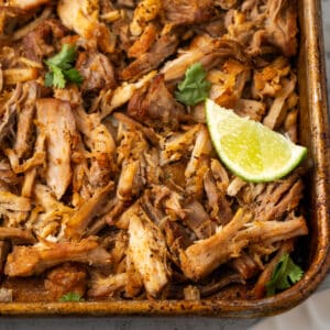 Crispy pork carnitas on a sheet pan garnished with lime and cilantro.