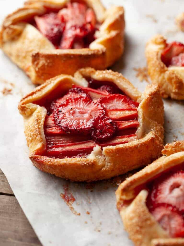 Mini strawberry rhubarb galettes sitting on a baking sheet.