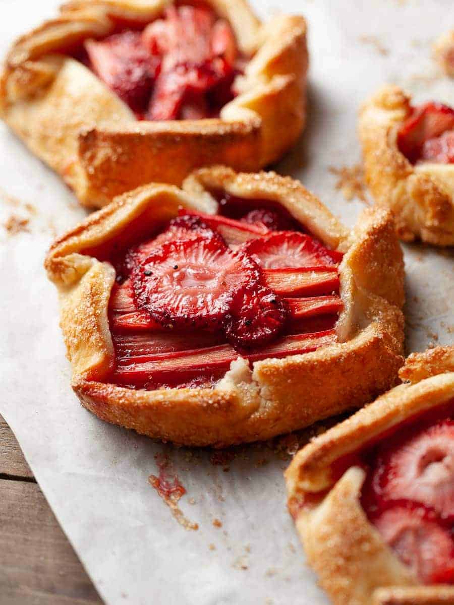 Several mini strawberry rhubarb galettes on a baking sheet.