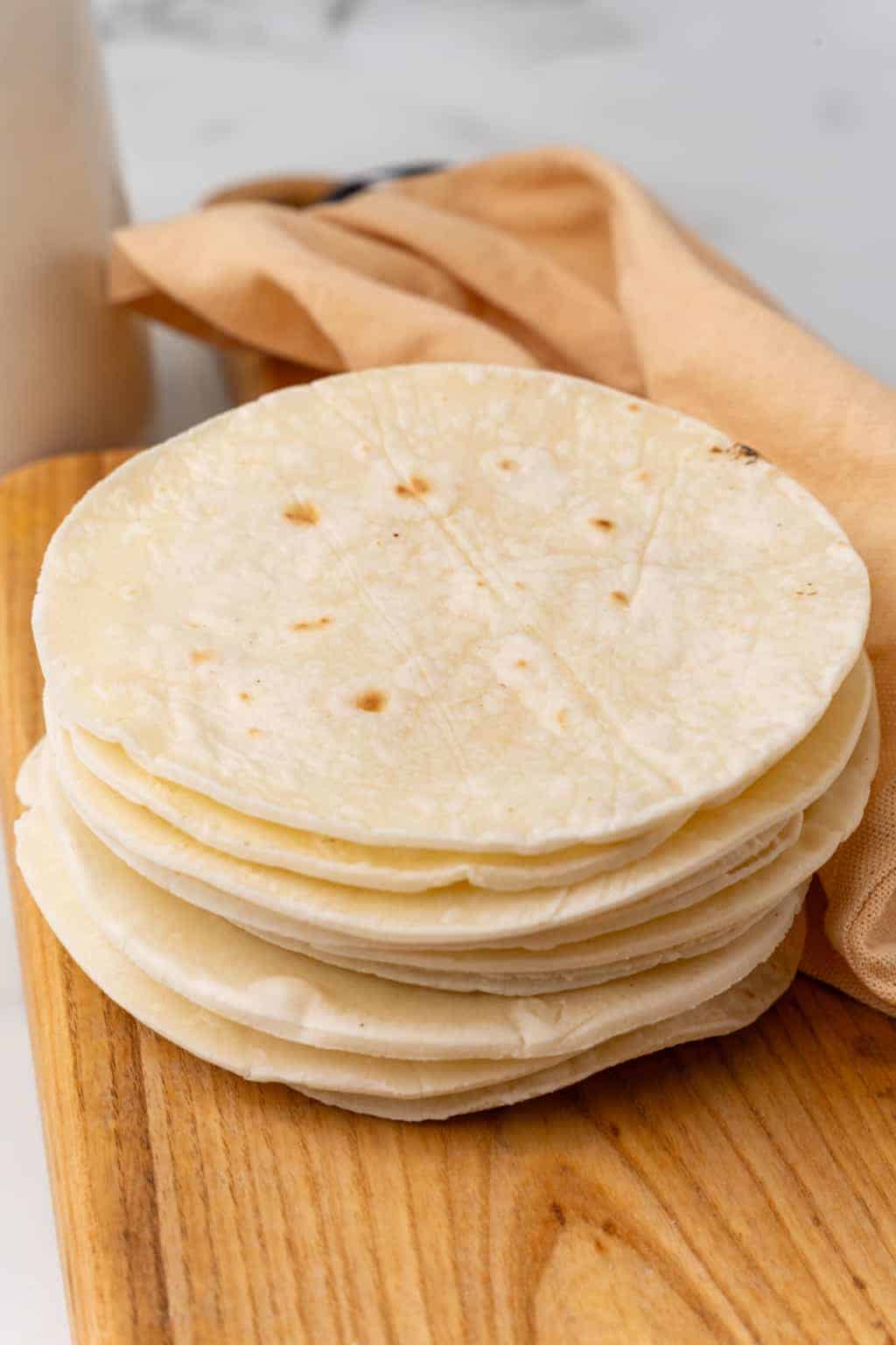 A stack of gluten free tortillas sitting on a wood cutting board.