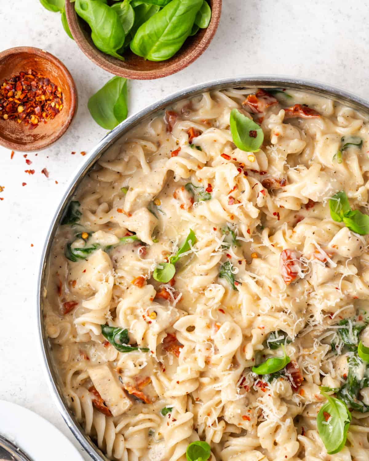 A pan filled with marry me chicken pasta that has been garnished with basil leaves, red pepper flakes and freshly grated cheese.