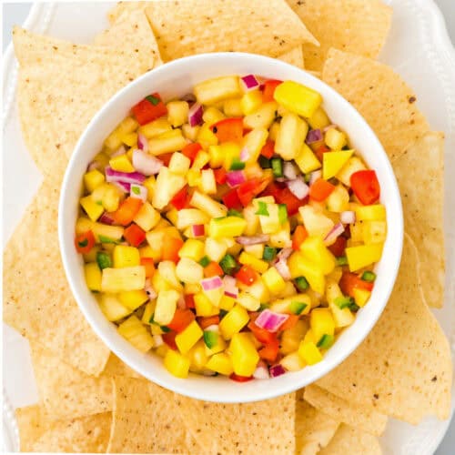 A bowl of pineapple mango pico de gallo surrounded by a plate of corn chips.