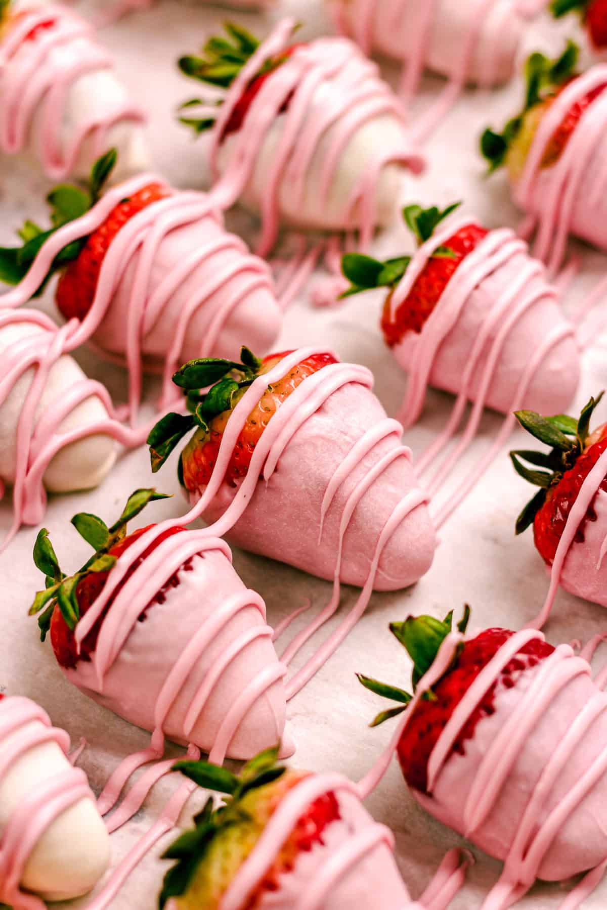 Strawberries dipped in pink hued white chocolate sitting on a baking sheet.