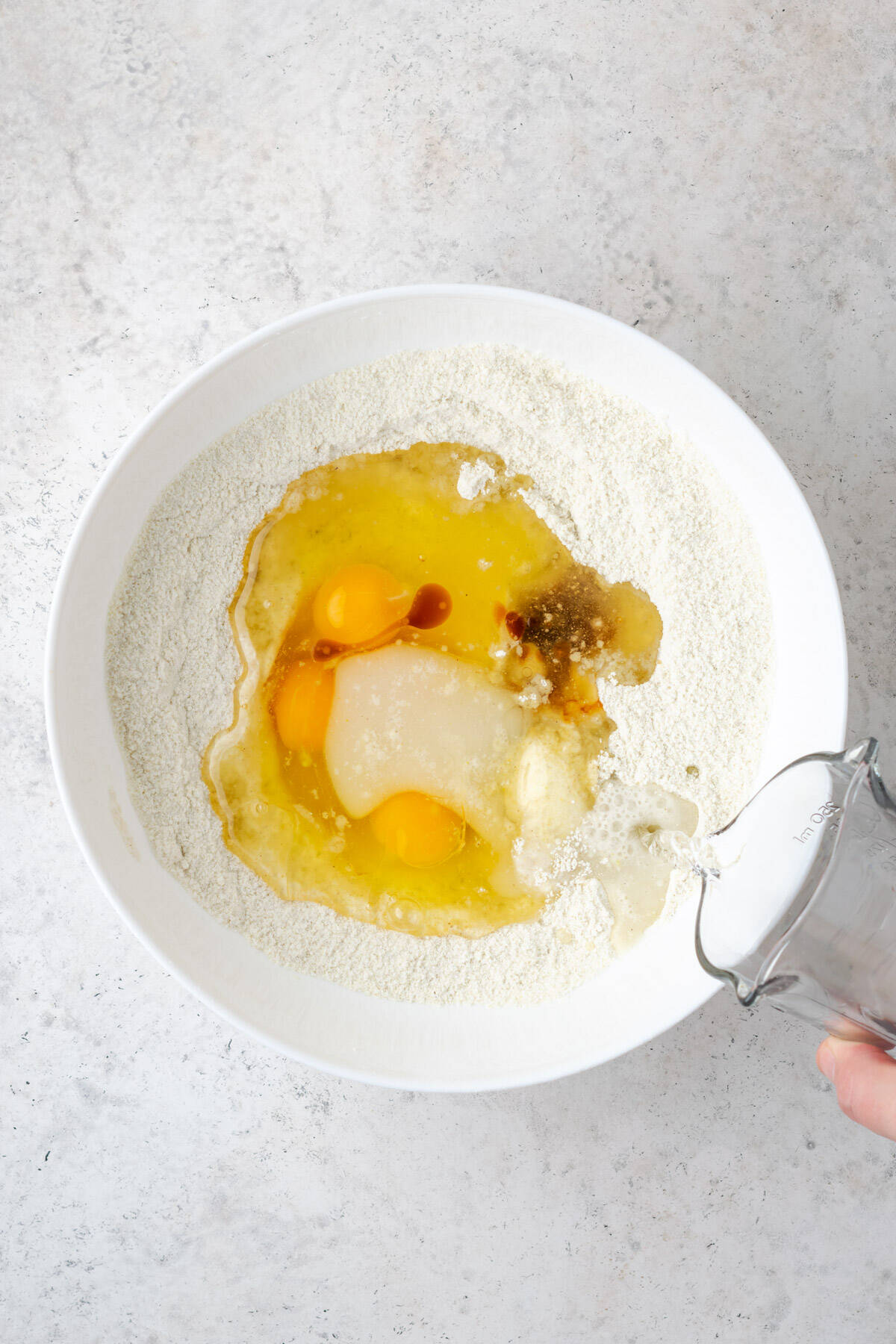 Eggs, oil, vanilla extract, almond extract and water being added to the mixing bowl with the dry ingredients.