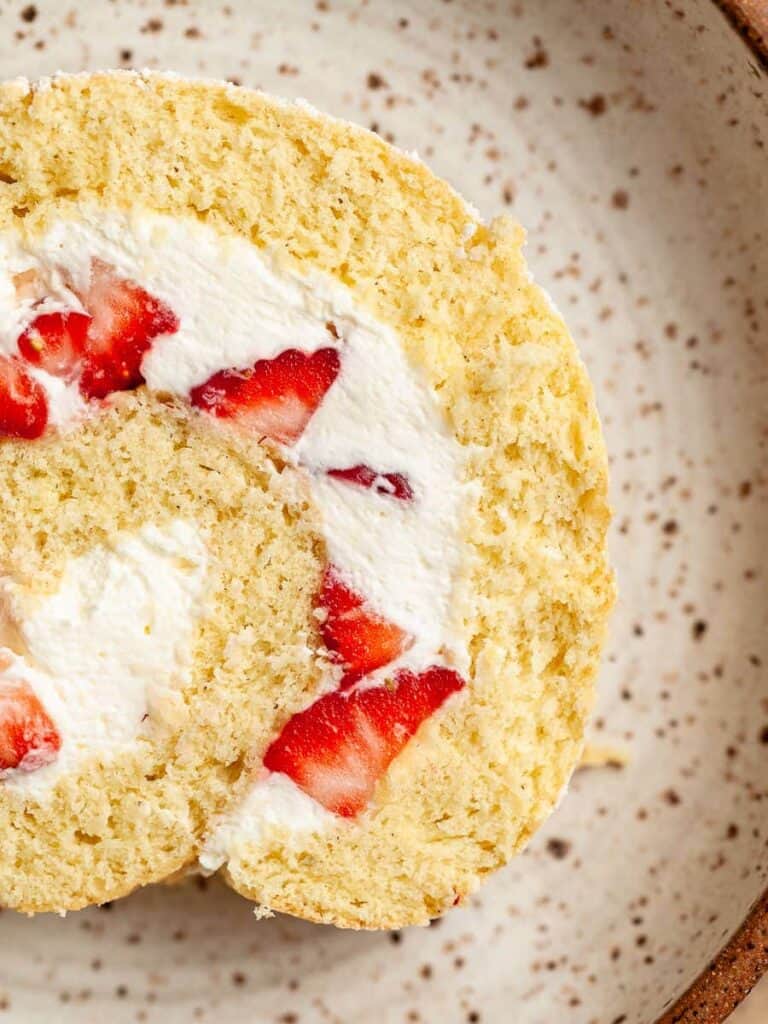 A slice of strawberry cake roll on a white speckled plate.