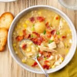 A bowl of chicken corn chowder topped with bacon pieces and chives.