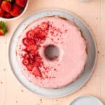 A strawberry pound cake on a white serving plate sitting on a pink table.